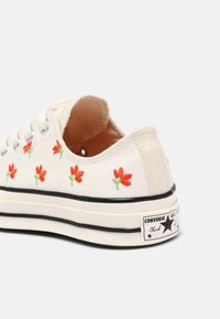 Plátěné tenisky s vyšitými červenými květinami, krémové barvy, černá gumová podrážka a klasické branded Converse na patě.