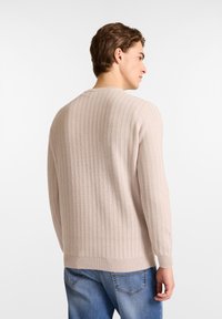 Beige gerippter Pullover mit langen Ärmeln, Rundhalsausschnitt und umgeschlagenen Säumen, aus weichem Strickmaterial gefertigt. Keine auffälligen Muster oder Details.