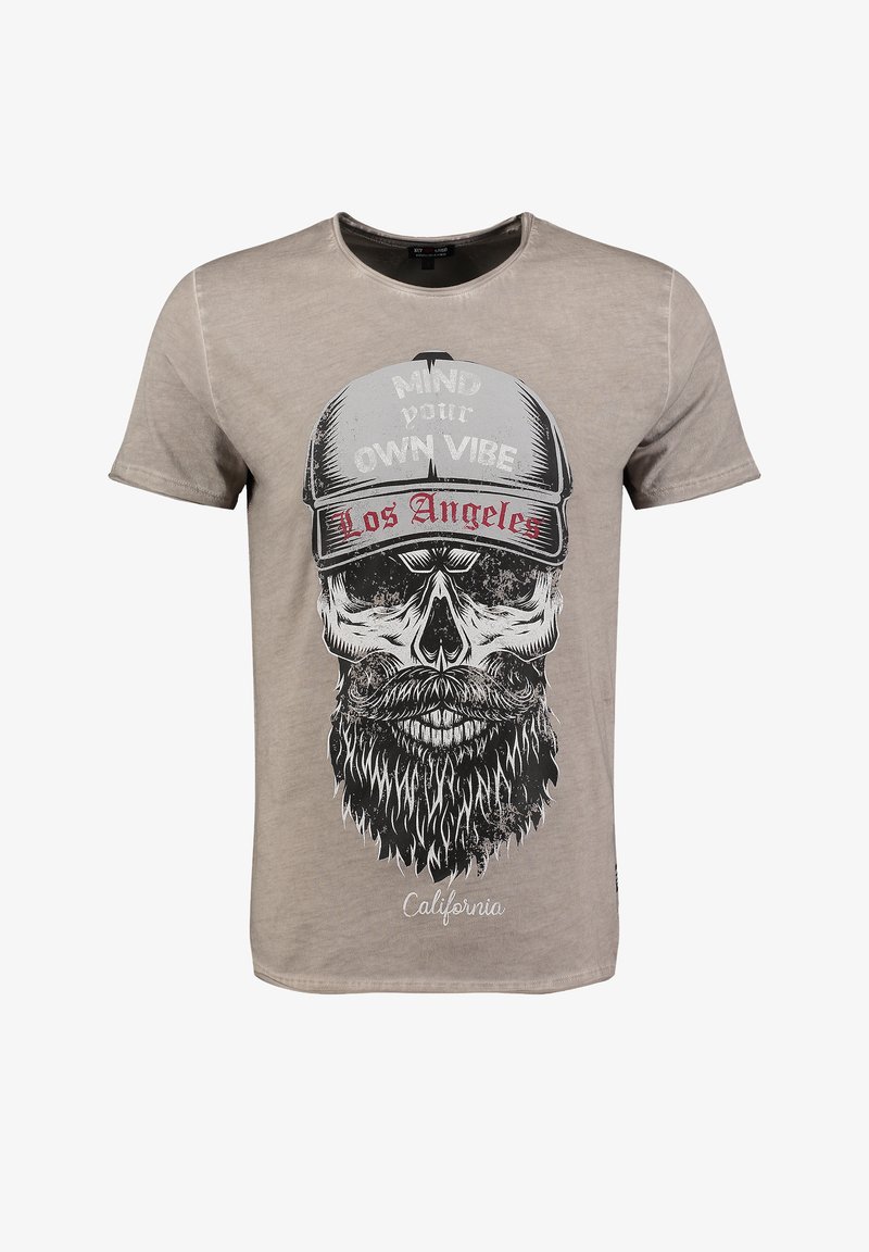 T-shirt en coton beige avec un graphique de crâne noir portant une barbe et une casquette, le texte inclut "Occupe-toi de ta propre ambiance" et "Los Angeles."