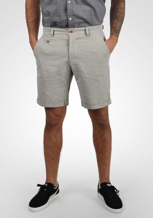 Lys grå shorts lavet af tekstureret stof, med foldet kant, knaplukning og to sidelommer. Båret med sorte sneakers.