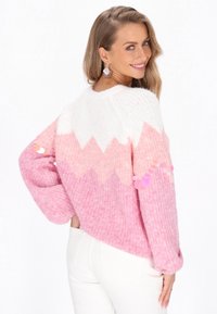 Rosa gestrickter Pullover mit einem weißen Zickzackmuster, langen Ärmeln und strukturiertem Stoff. Verziert mit runden, glänzenden Akzenten an den Ärmeln.
