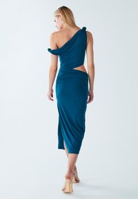 Obleka modre zelenkaste barve, oprijeta, z rameni brez naramnic, stranskim izrezom in naborki. Dolžina do sredine meč, z razporkom, izdelana iz gladkega blaga.