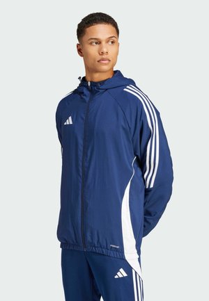 Marineblauwe ritsjack met capuchon, voorzien van witte zijkanten en logo-accenten. Lichtgewicht, gladde textuur met elastische zoom.