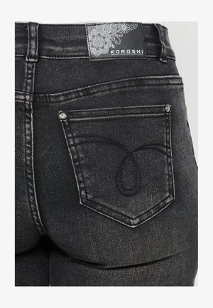 Fekete farmernadrág textúrált anyagból, hátul különleges dizájnnal ellátott zsebbel és márkajelzéssel a derékpánton.