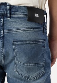 Tmavě modré džíny z denimu s jemným vybledlým vzhledem, kožená nášivka LTB na pasu, viditelný detail prošití zadní kapsy.