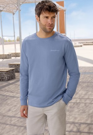 Lange mouwen, lichtblauw shirt van zachte stof met een ronde hals en geborduurd logo op de borst, gecombineerd met beige shorts.