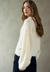 Krēmkrāsas adīts džemperis ar brīvu piegriezumu, plašām piedurknēm un ribiņu apakšdaļu, saskaņots ar tumšiem denima džinsiem. Mīksta tekstūra un patīkams izskats.