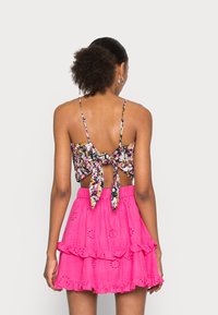 Top de flores com padrões em preto, rosa e amarelo, apresentando um design com laço nas costas. Combinado com uma saia rosa em camadas com detalhes de ilhós.