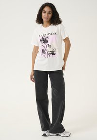 T-shirt blanc avec un graphique floral en noir et rose, avec le mot "FRAÎCHEUR" affiché en évidence. Assorti à un pantalon large gris foncé.