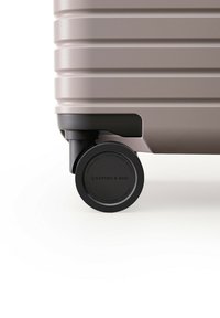Harde koffer in lichtbeige met een ribbeltextuur. Voorzien van een zwarte prestatiekogel met branding op de zijkant.