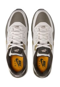 Zapatillas Nike Air con parte superior de malla blanca y cuero, detalles grises y una plantilla amarilla con el logo. Cordoneras planas blancas y un collar acolchado.