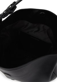 Zwarte leren handtas met verstelbare schouderband, open bovenkant die een zachte zwarte stofvoering en een binnenzak met subtiele branding onthult.