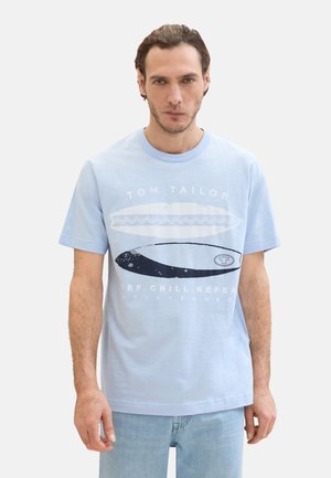 Camiseta de algodón azul claro con mangas cortas, que presenta un diseño gráfico de tablas de surf y el texto “TOM TAILOR” en blanco y negro.