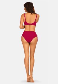 Czerwony komplet bikini, składający się z majtek z wysokim stanem z wiązaniami po bokach i usztywnionego topu z regulowanymi ramiączkami, wyeksponowany z tyłu.