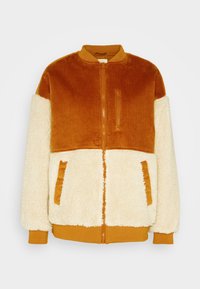 Chaqueta bomber de corduroy y forro polar con parte superior en un cálido color naranja, parte inferior en crema, bolsillos con cremallera, puños acanalados y cierre de cremallera. Textura suave en general.