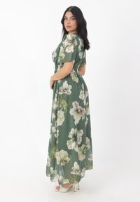 Robe maxi florale verte avec des fleurs blanches et lavande, manches courtes bouffantes, et taille smockée ; tissu léger et transparent.