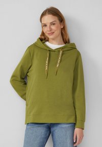 Oliwkowy sweatshirt z kapturem z miękkiego materiału, z sznurkiem do regulacji i nadrukowanym tekstem, o luźnym kroju. Noszony z jasnoniebieskimi dżinsami.