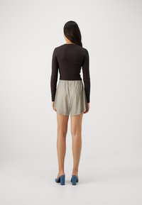 Long-sleeve brown top paired with light blue and tan striped shorts, featuring an elastic waistband and a flared cut. Blue block-heeled shoes.