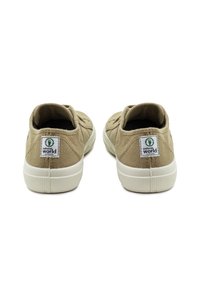 Zapatillas de lona beige de diseño bajo, con una suela de goma blanca. La etiqueta trasera dice "natural world" con un logo verde.