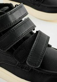 Baskets noires en cuir synthétique, avec plusieurs bandes Velcro et des coutures contrastées, dotées d'un bout arrondi et d'une semelle en caoutchouc crème.