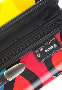 Maleta rígida con un diseño en rojo y negro, un acento amarillo, cierre con cremallera y un mecanismo de bloqueo aprobado por la TSA.