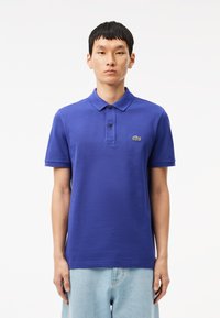 Camisa polo azul hecha de algodón texturizado, con un cuello clásico, una tapeta de tres botones y un pequeño logo verde en el lado izquierdo del pecho.