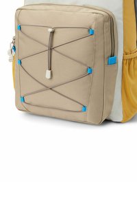 Mochila de tela beige con un bolsillo frontal texturizado, detalles de cordón elástico, acentos azules y un panel lateral de malla amarilla.