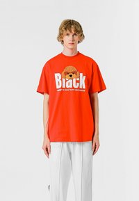 Camiseta de algodón roja con cuello redondo, que presenta un gráfico texturizado de la cara de un oso encima de un texto en bold que dice "Black". Manga corta.