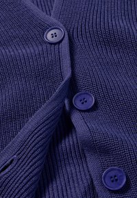 Nahaufnahme von blauem Strickstoff mit drei großen passenden blauen Vierlochknöpfen, die am gerippten Kleidungsstück befestigt sind.