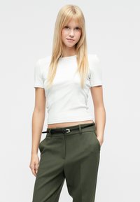 Biała obcisła koszulka z krótkim rękawem zestawiona z oliwkowozielonymi spodniami z wysokim stanem i czarnym paskiem ze srebrną klamrą. Gładka tekstura.