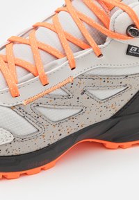 Zapato de senderismo impermeable gris con cordones naranjas, acentos moteados, parte superior de malla texturizada y suela de goma negra con agarre contorneado.