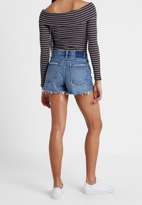 Shorts de mezclilla con dobladillo deshilachado, de cintura alta y dos bolsillos traseros. Combinados con una blusa de manga larga sin hombros de rayas blancas y negras.