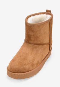Stivale alla caviglia in suede marrone con una morbida fodera bianca, punta arrotondata e suola in gomma texturizzata. Presenta un pratico tassello per una facile calzata.