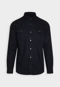 Chemise noire à manches longues en coton, avec un col boutonné et deux poches poitrine avec fermetures à pression. Texture lisse, coupe ajustée.