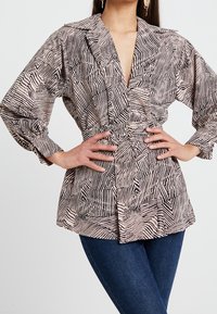 Blouse légère à motifs rose et noir, avec un profond décolleté en V, des manches longues, une taille cintrée et un col structuré.