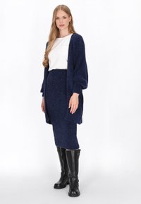 Granatowy, teksturowany sweter kardigan z luźnymi rękawami, w połączeniu z dopasowaną spódnicą do kolan. Modelka ma na sobie wysokie czarne botki.