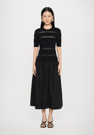 Top negru din tricot, cu dungi texturate, mâneci scurte și fustă midi neagră, fluidă. Purtați cu sandale negre cu barete.
