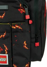 Zwarte LEGO-rugzak met rood en oranje vlammenpatroon, rode ritstrekkers en een LEGO-logopatch op het voorvak.