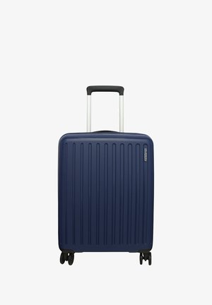 Valigia rigida blu navy con texture a coste verticali, manico telescopico argentato e quattro ruote nere per la mobilità.