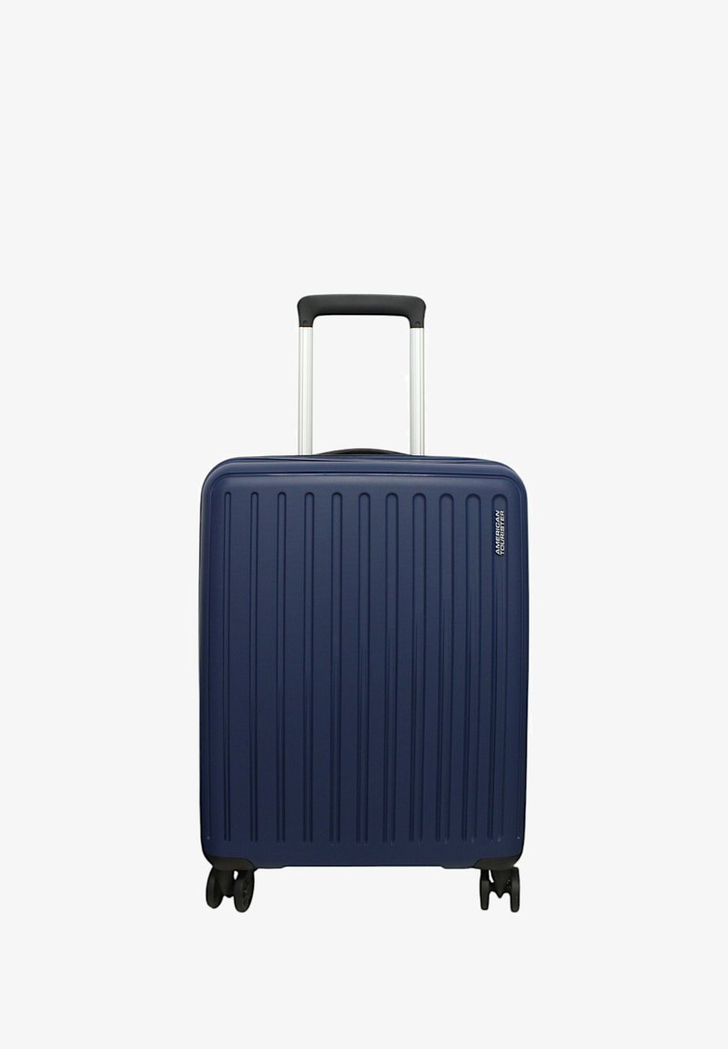 Valigia rigida blu navy con texture a coste verticali, manico telescopico argentato e quattro ruote nere per la mobilità.