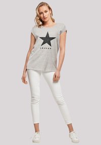 Gray t-shirt with a large black star graphic and five smaller stars below. Paired with white skinny jeans and white sneakers.