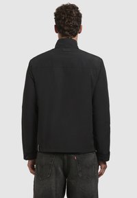 Black jacket with a high collar, snap-button cuffs, and a straight design. Fabric appears smooth with a matte finish.