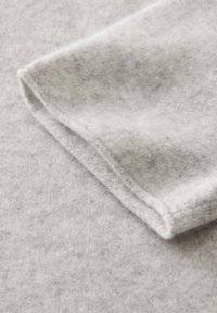 Gros plan sur un tissu doux de couleur gris clair avec un bord replié, montrant sa texture de tricot fine et les détails de couture.