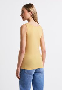 Top corto amarillo elegante con escote redondeado, hecho de una tela suave y elástica, combinado con jeans de mezclilla azul claro.