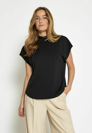 Haut noir à manches courtes avec un col haut, texture lisse et coupe décontractée, associé à un pantalon beige à jambes larges.