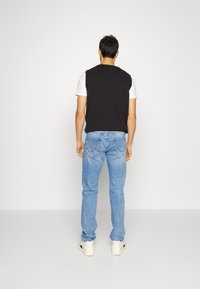 Top negro sin mangas sobre una camiseta blanca, combinado con jeans azul claro y zapatillas de un color claro. Los jeans presentan un sutil detalle en los bolsillos traseros.