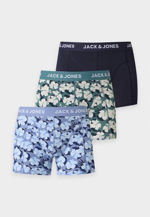 Muskuløs mand, der står barfodet iført blå blomstrede boxershorts med Jack & Jones taljebånd, mod en ensfarvet lys baggrund.
