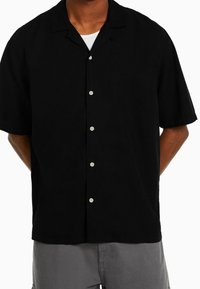 Black short-sleeve button-up shirt with a relaxed fit, featuring a collar and white buttons. The fabric appears smooth and lightweight.