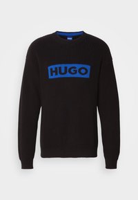 Pull noir en maille à manches longues et col rond, avec un patch rectangulaire bleu portant le texte "HUGO" sur la poitrine.