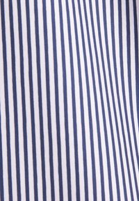 Gros plan sur un tissu blanc avec des rayures verticales bleu marine uniformément espacées, créant un motif propre et classique.